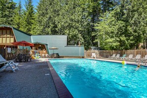 A swimming pool with lounge chairs and a deck area, surrounded by a wooden fence and trees.