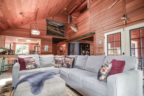 A log cabin interior with a large L-shaped sofa, a dining area, and a kitchen.