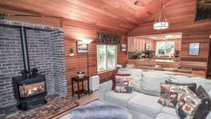 Interior acogedor de una cabaña con chimenea, sofá y zona de cocina.