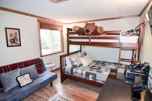 A bunk bed with a cartoon character headboard, a sofa with a plaid blanket, and a small round table.