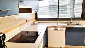 Moderni keittiö, jossa on sisäänrakennettu astianpesukone, liesi ja ikkuna, jossa on sälekaihtimet.