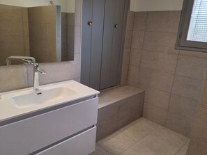 Bathroom features a vanity with a mirror and cabinet, a shower area, and a window with blinds.