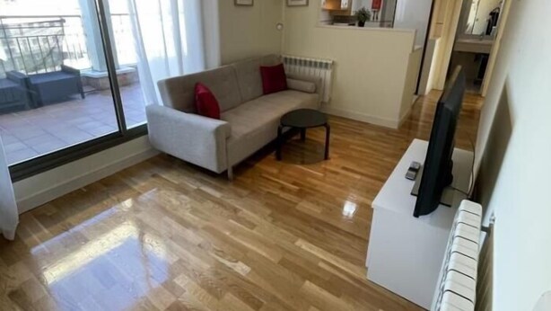 Een moderne woonkamer met een bank, een kleine tafel en een televisie. Er is een groot raam dat natuurlijk licht en uitzicht op het exterieur biedt.