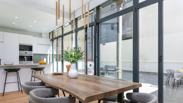 A modern kitchen with a wooden dining table, grey chairs, and pendant lighting.
