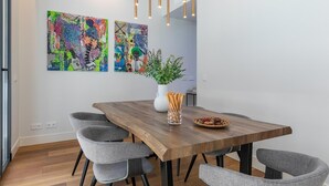 A modern dining area with a wooden table, grey upholstered chairs, and two abstract paintings on the wall.