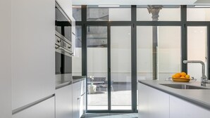 A modern kitchen with a large window, a sink, and a bowl of fruit on the counter.