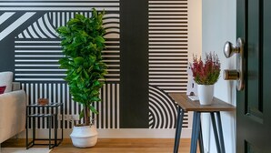 Un salón moderno con una pared a rayas negras y blancas, una planta en maceta, una mesita con un jarrón y una puerta.