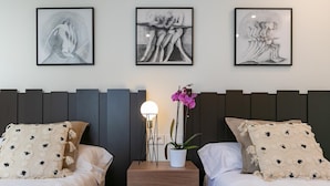 Habitación de hotel con dos camas, una mesita de noche con lámpara y tres obras de arte enmarcadas en la pared.