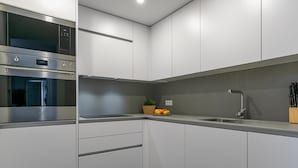 Una cocina moderna con electrodomésticos de acero inoxidable, armarios blancos y encimera gris.