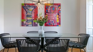 Un comedor con una mesa de vidrio, sillas negras, un jarrón blanco con flores y dos cuadros abstractos en la pared.
