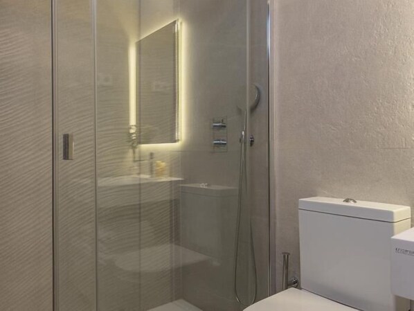 Un baño moderno con cabina de ducha de vidrio, un lavabo blanco y un inodoro.