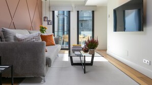 Un salon moderne avec un canapé gris, une table basse en verre et un téléviseur à écran plat fixé au mur.