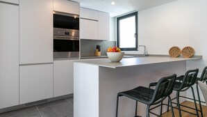Une cuisine moderne avec des meubles blancs, un four encastré, un grand îlot central doté de tabourets de bar et une fenêtre au-dessus de l’évier.