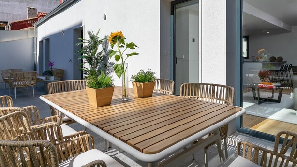 Une terrasse extérieure avec une table en bois et des chaises en osier, entourée de plantes en pot.