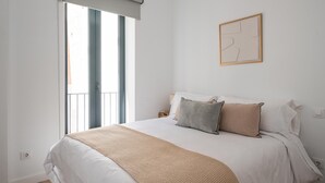 A bedroom with a bed, a window with blinds, a wall-mounted picture, and a power outlet.