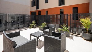 An outdoor seating area with wicker furniture and potted plants, enclosed by a black perforated fence.