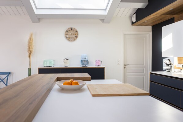 A modern kitchen with a skylight, a wooden dining table, a bowl of fruit, and a cutting board.