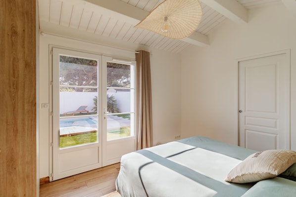 A bedroom with a bed, a door, and a view of a swimming pool through a sliding glass door. - La Dionysienne piscine privée (Saint-Denis-d´Oléron)
