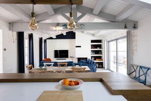 A spacious living room with a large TV, blue sofas, and a wooden dining table with a fruit bowl. - La Dionysienne piscine privée (Saint-Denis-d´Oléron)