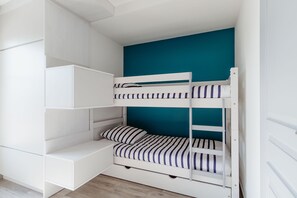 A bunk bed with a teal wall behind it, white storage units, and a wooden floor.