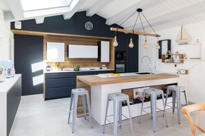 A modern kitchen with a central island, bar stools, and pendant lighting.