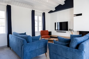 A modern living room with blue sofas, a wooden coffee table, and a flat-screen TV mounted on the wall. - La Dionysienne piscine privée (Saint-Denis-d´Oléron)