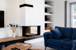 A modern living room with a flat-screen TV, a blue sofa, a wooden coffee table, and a white vase with dried plants.
