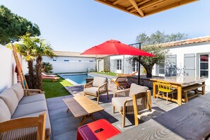 Eine Terrasse mit Gartenmöbeln, einem Swimmingpool und einem roten Sonnenschirm.