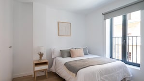 A bedroom with a bed, bedside table, lamp, and a window with a view.