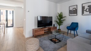 A modern living room with a flat-screen TV, a blue armchair, a grey sofa, and a potted plant.
