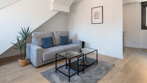 A modern living room with a grey sofa, a glass coffee table, and a potted plant.