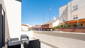 A modern outdoor patio with wicker furniture, a tiled floor, and a view of neighboring buildings and a clear sky.