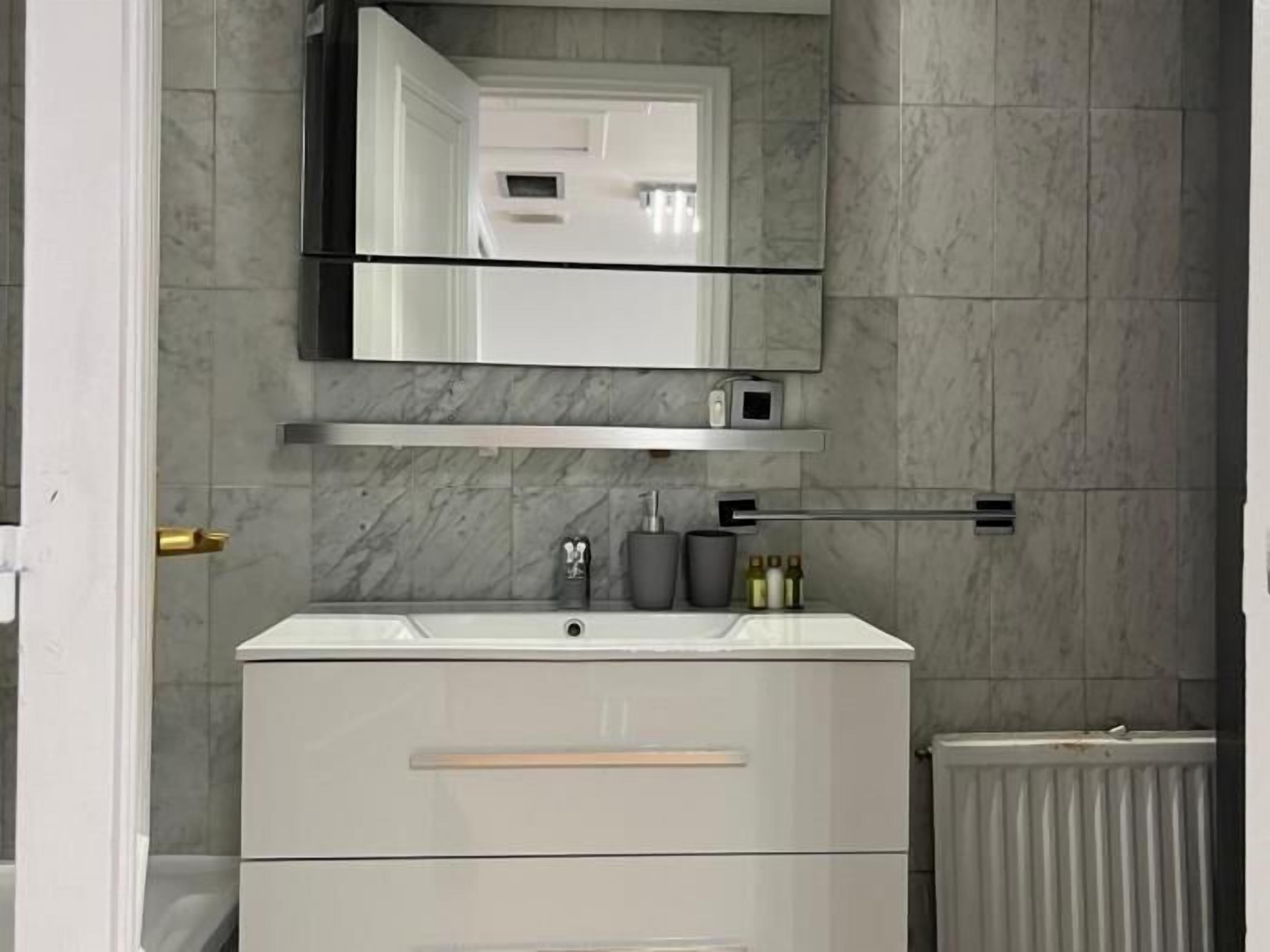 Un bagno con un mobile lavabo bianco, uno specchio sopra e un termosifone sotto.