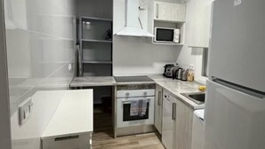 Una cocina compacta con armarios blancos, un microondas, una estufa y un lavamanos.