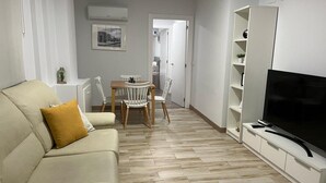 Una sala de estar moderna con un sofá, una mesa de comedor con sillas, un televisor y una cocina al fondo.