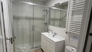 Un baño moderno con cabina de ducha de vidrio, un lavabo blanco y un inodoro.