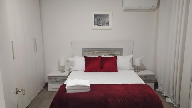 Ein modernes Hotelzimmer mit einem großen Bett, weißen Wänden, einer roten Tagesdecke und einem gerahmten Bild an der Wand.