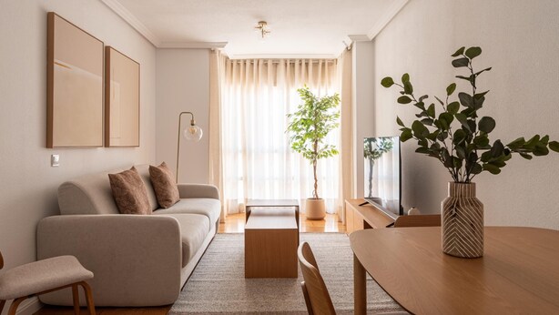 A modern living room with a sofa, coffee table, and dining table. There is a potted plant and a TV on a stand. - Las Tablas - 1 Bedroom with sofa bed and terrace (Madrid)