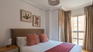 A neatly arranged bedroom with a large bed, a bedside table, and a window with curtains. - Las Tablas - 1 Bedroom with sofa bed and terrace (Madrid)