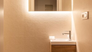 Un baño con un lavamanos blanco, un espejo encima y un mueble de madera debajo.