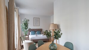 Una habitación de hotel moderna con cama, mesita de noche, lámpara y mesa de comedor con sillas.