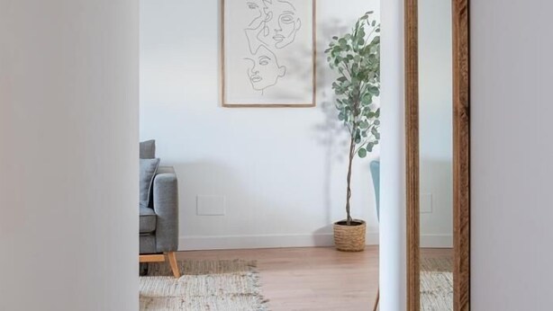 Una sala de estar minimalista con un sofá gris, una obra de arte abstracto enmarcada, una planta en maceta y una alfombra tejida.