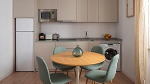 Une cuisine compacte équipée d’un four à micro-ondes, d’un grille-pain, d’une bouilloire, d’un évier et d’un lave-linge. On y trouve une table ronde en bois, accompagnée de quatre chaises.