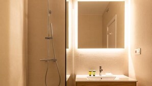 Une salle de bain avec un meuble-lavabo en bois, un miroir, une douche et un porte-serviettes.