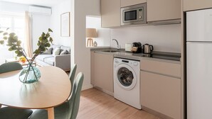 Een functionele keuken met een wasmachine, een magnetron en een spoelbak. Er is een eethoek met een tafel en stoelen.