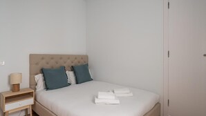 Een keurig opgemaakt bed met een geborduurde hoofdbord, twee kussens en opgevouwen handdoeken op een witte matras.