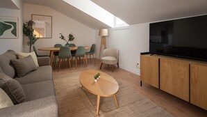 Ein modernes Wohnzimmer mit einer Couch, einem Couchtisch, einem Essbereich mit Stühlen, einem Fernseher und einer Lampe.