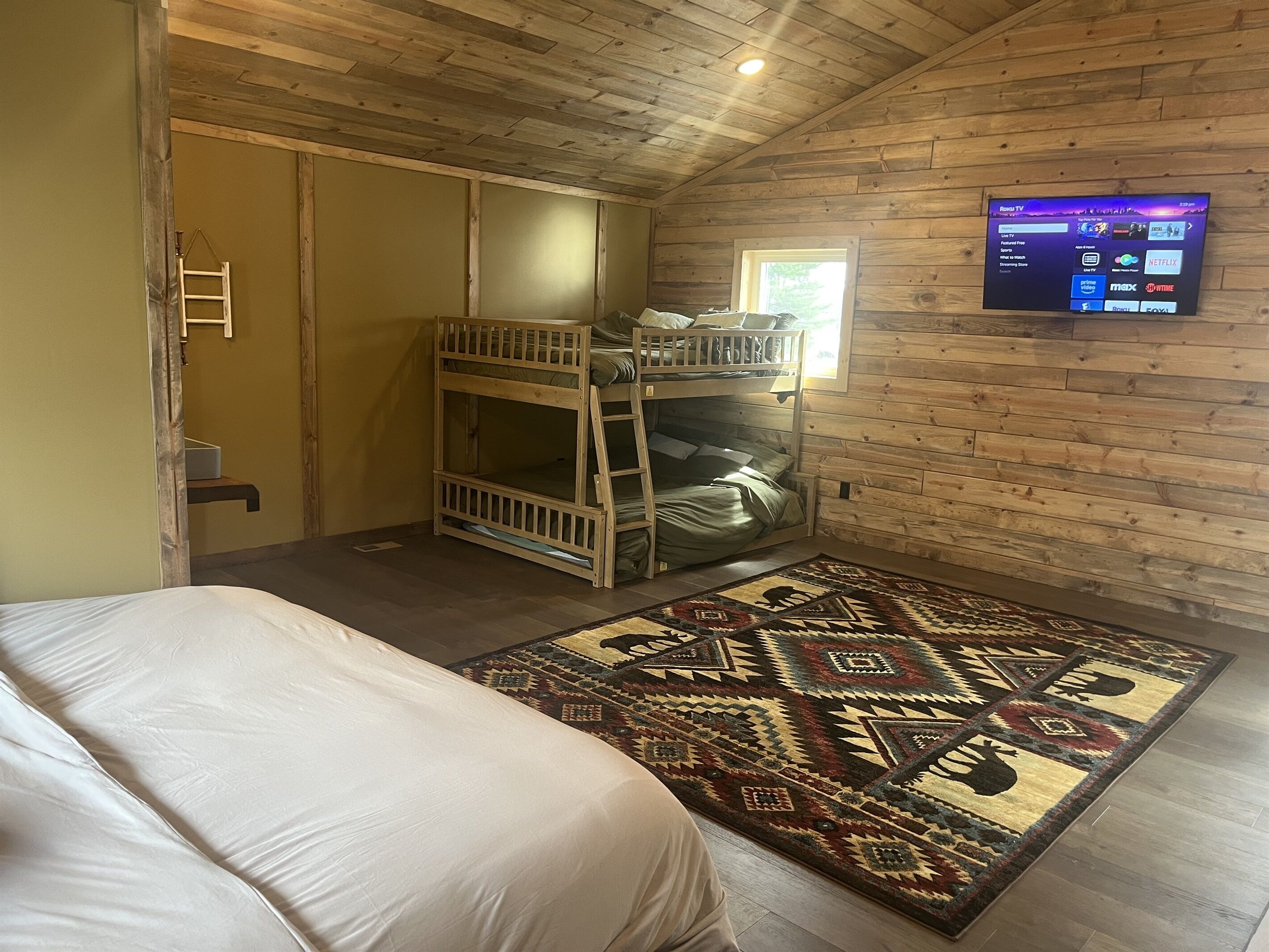 A room with a bunk bed, a television mounted on the wall, and a patterned rug on the floor.