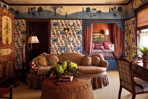 A cozy room with a sofa, a chair, a table with a vase of flowers, and a bed with a red blanket.