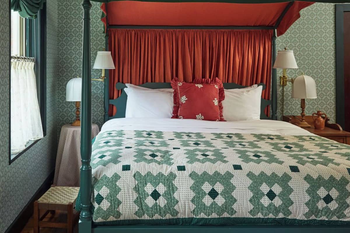 A four-poster bed with a green canopy, red curtains, and a patterned quilt.